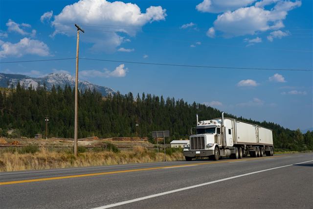 White semi truck pulling two trailers on a mountain highway