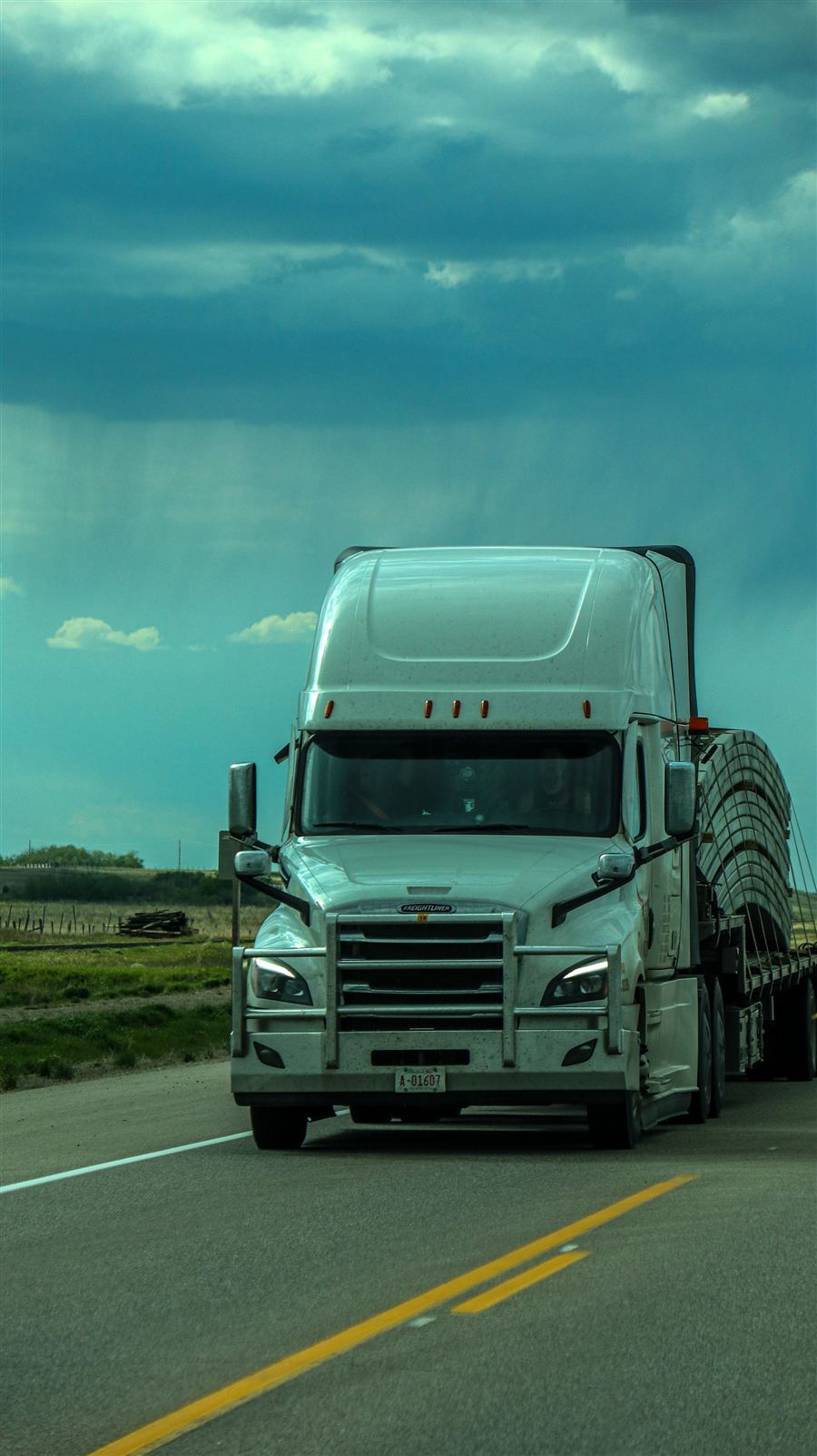 White semi truck hauling a flatbed load under a stormy sky